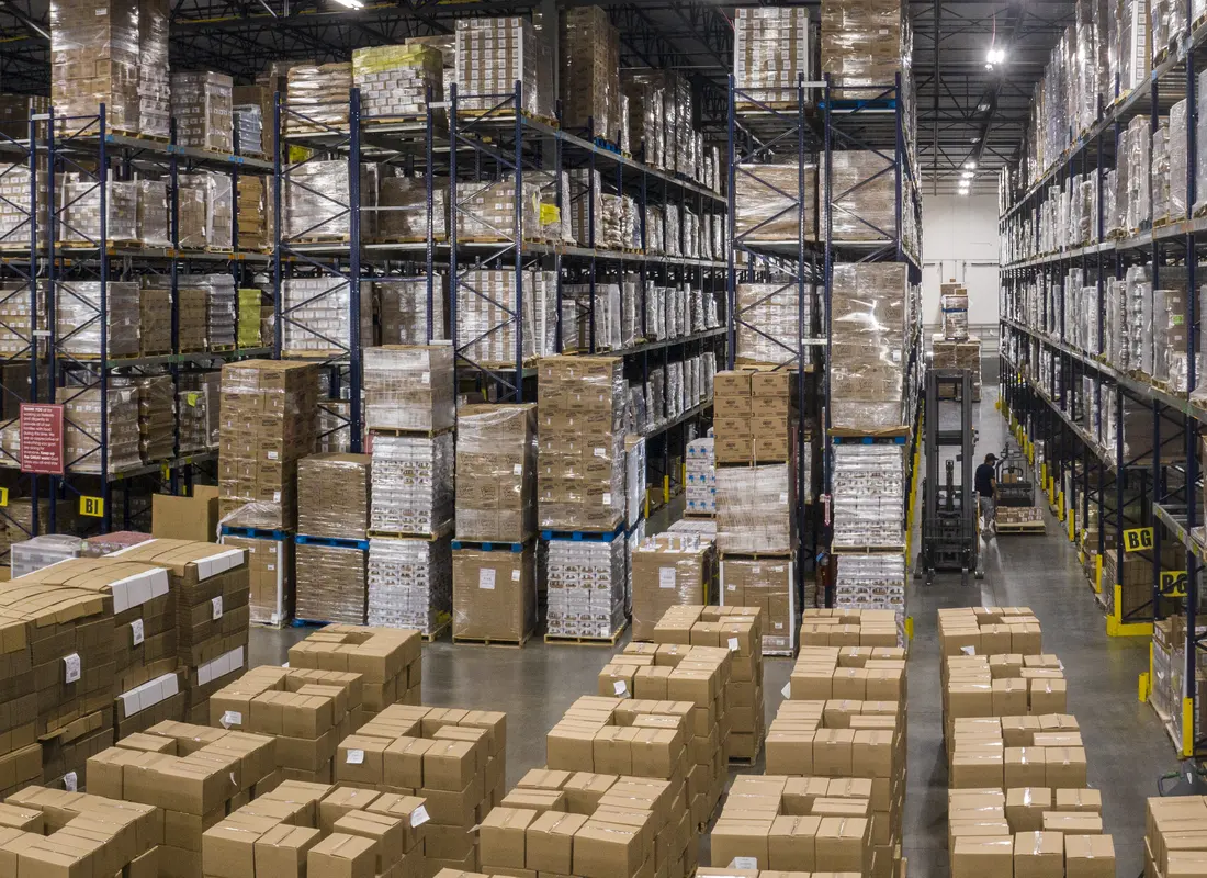 High-bay pallet racking in a distribution warehouse, with cases staged on the floor for picking.